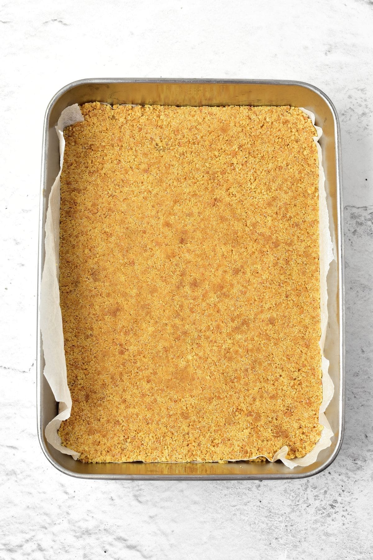 Baked graham cracker base in metal baking pan.