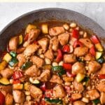 Chicken cubes and veggies in a pan.