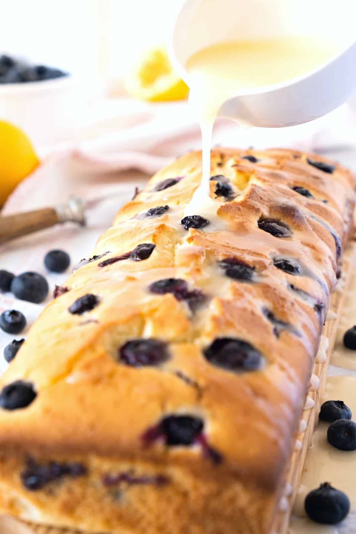 Pouring lemon glaze over a loaf of gluten-free blueberry bread.