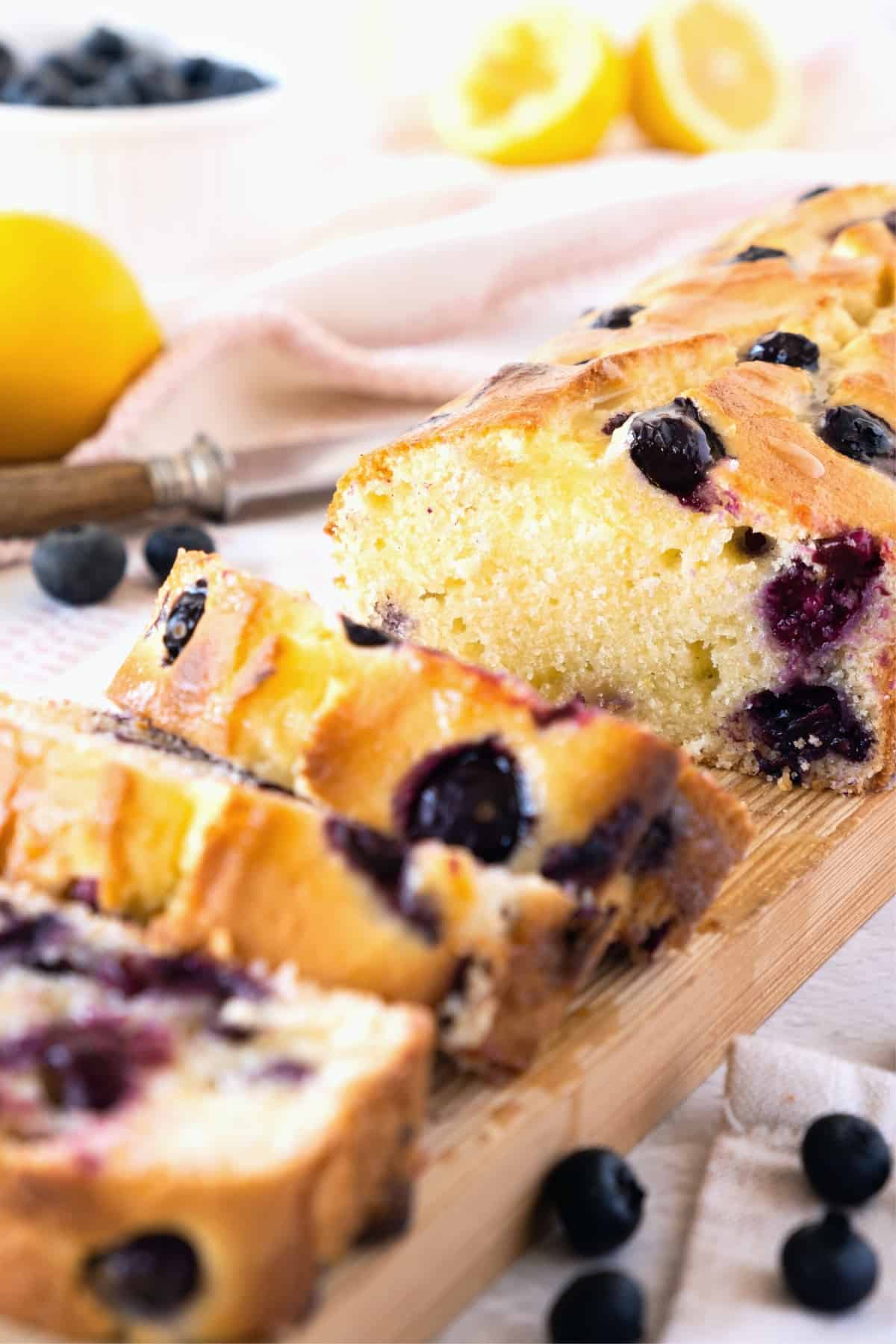 A sliced loaf of lemon blueberry bread on wooden board.