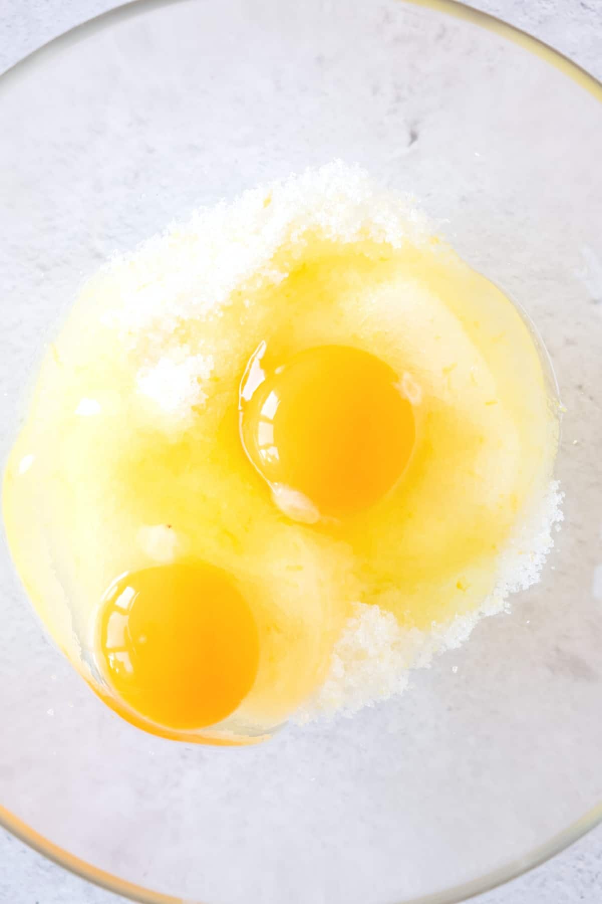 Two eggs and sugar in a glass bowl.