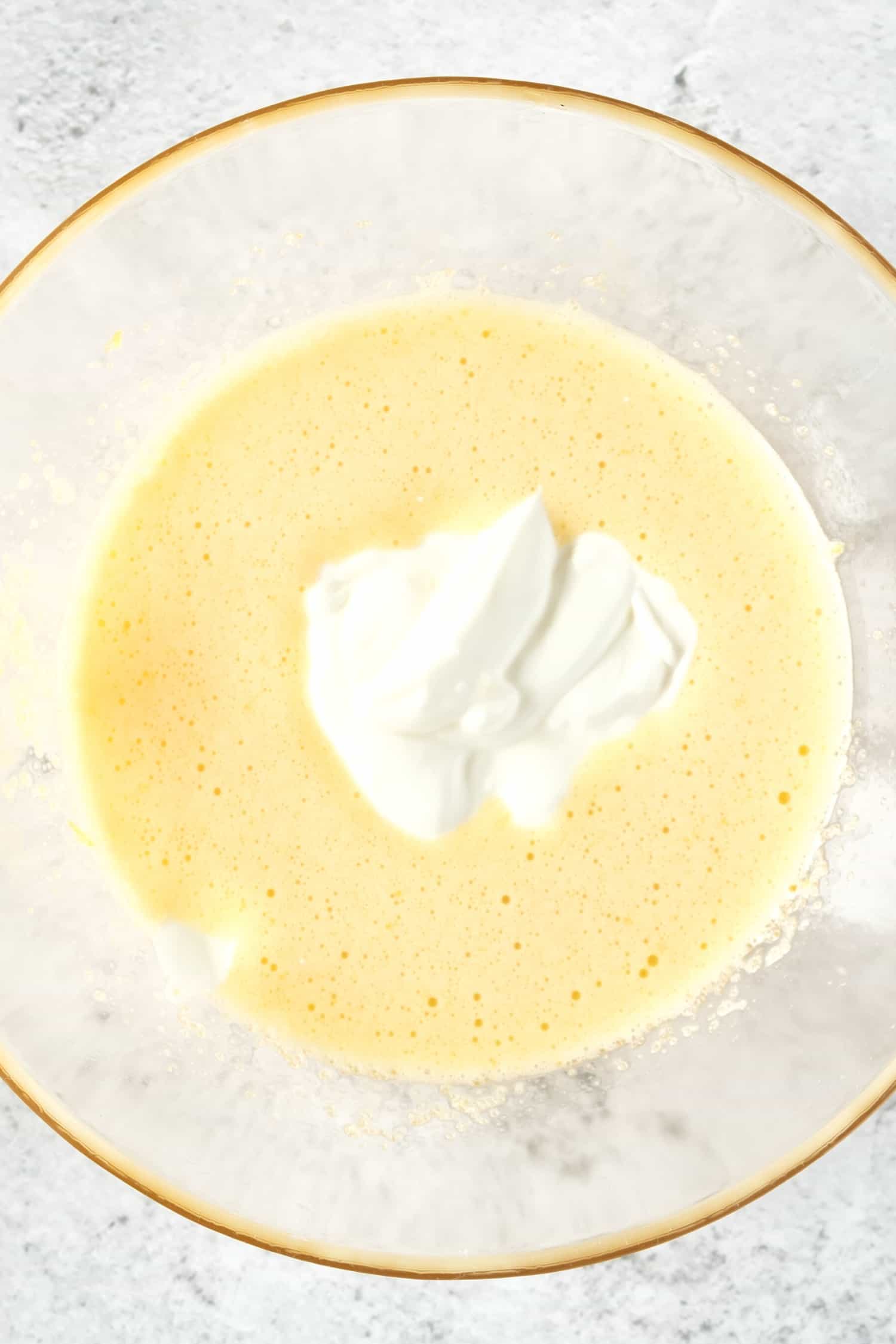 Yogurt on top of pale yellow cake batter in a bowl.