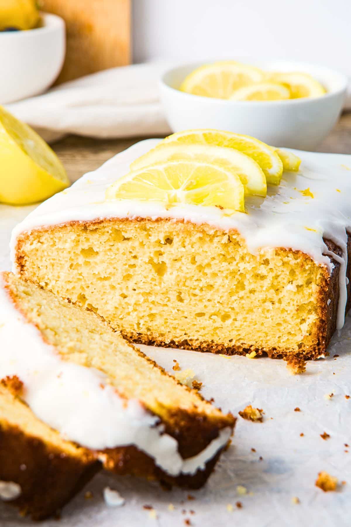 Half-sliced loaf of gluten-free lemon drizzle cake on parchment paper.