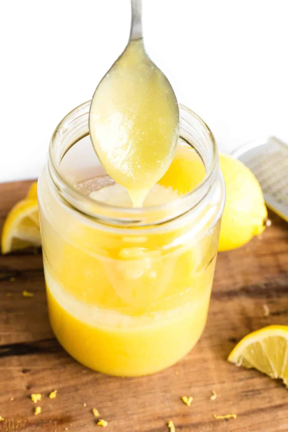 Holding up a spoonful of lemon curd from a jar.
