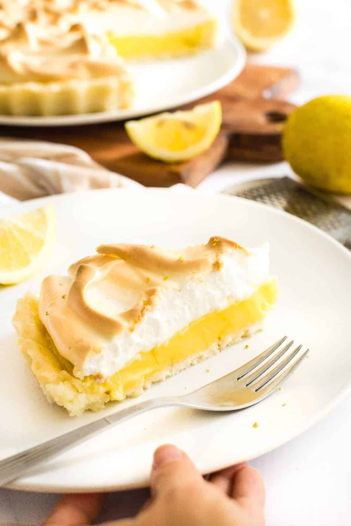 Hand reaching for a plate of gf lemon meringue pie.