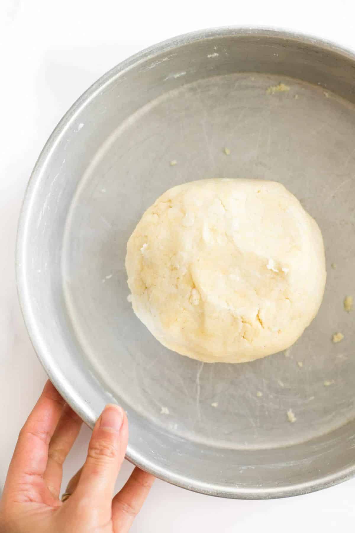 Hand holding a metal bowl with a ball of pie crust dough.