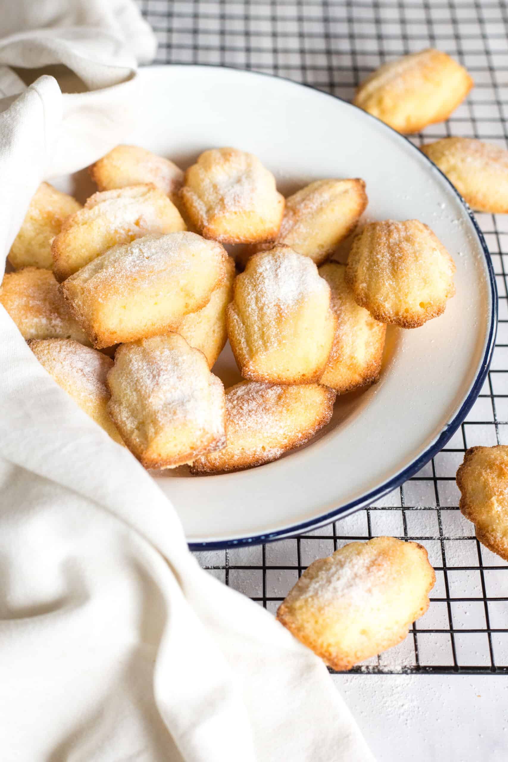 Gluten-free madeleines on a white place resting on a wire rack.