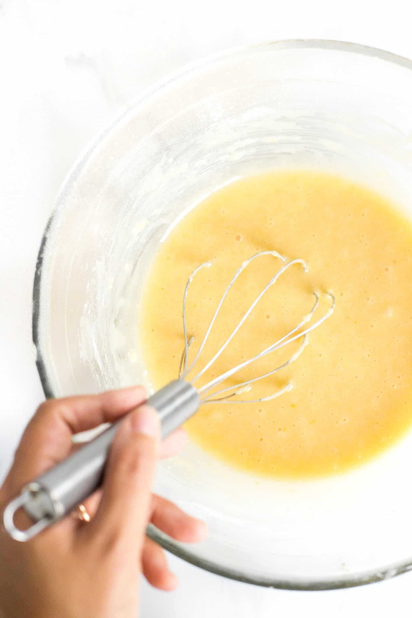 Whisking madeleine batter in a glass mixing bowl.