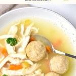 Top down view of a spoon in a bowl of matzo ball soup.