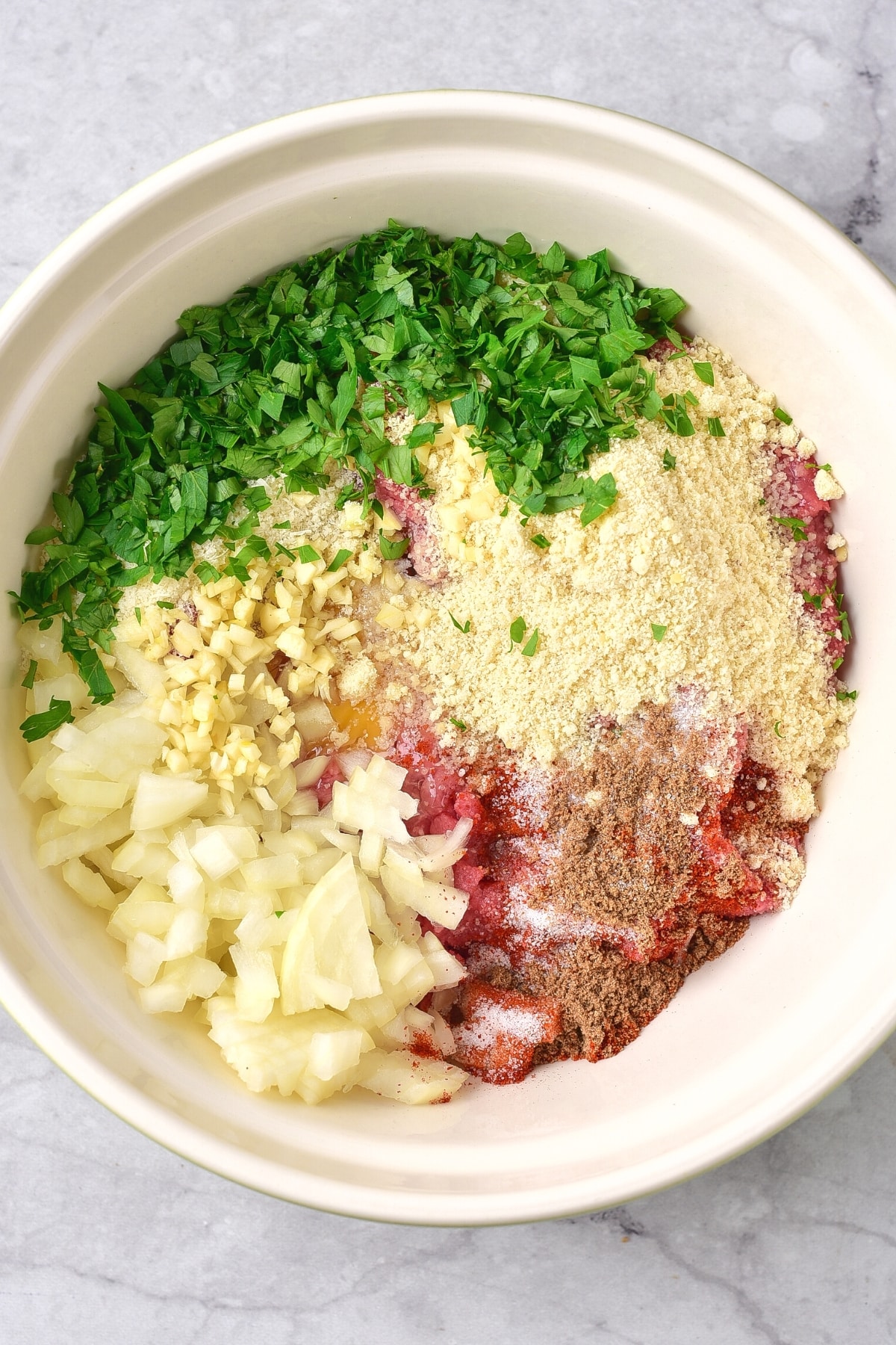 Ground beef, almond flour, parsley, minced garlic, diced onions and spices in a bowl.