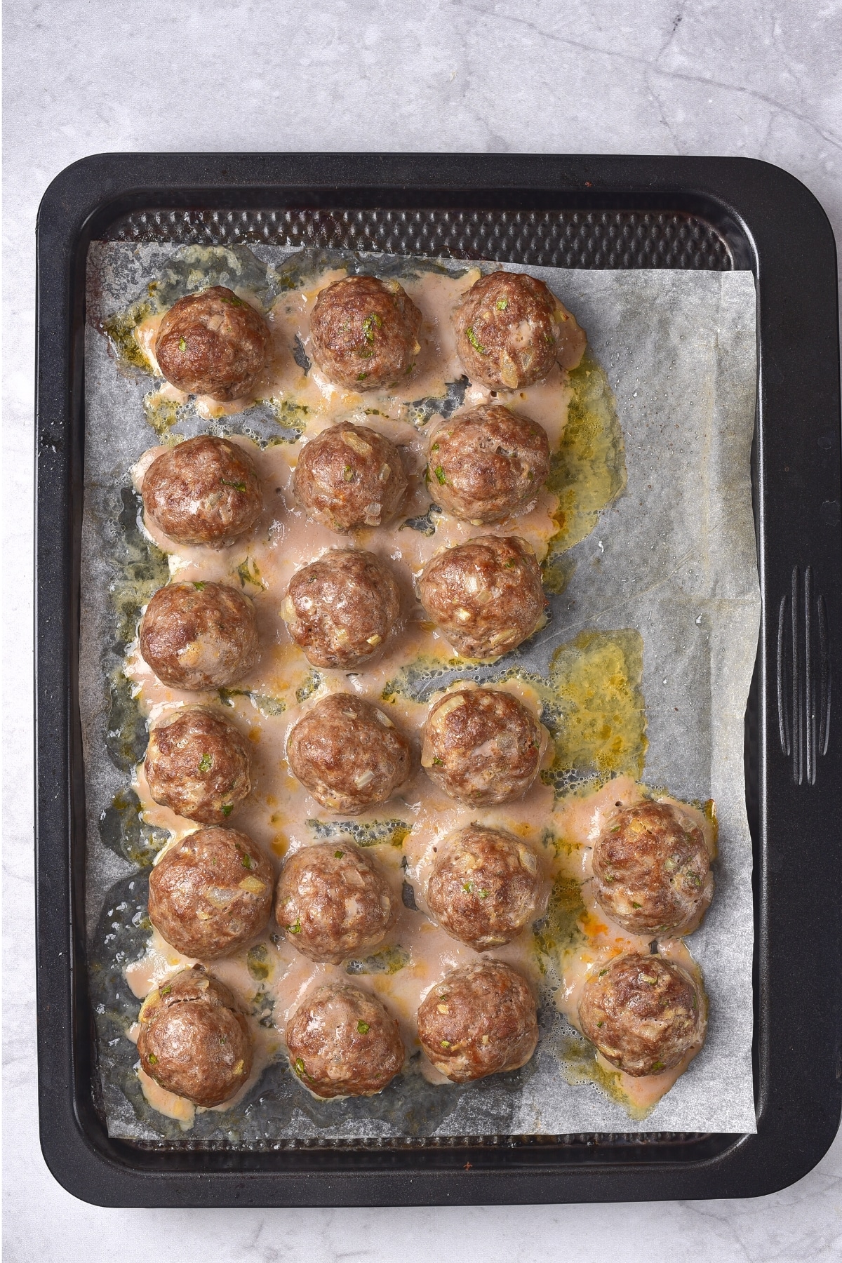 Cooked gf meatballs on parchment-lined baking sheet.