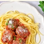 Meatballs and tomato sauce on top of a plate of spaghetti.