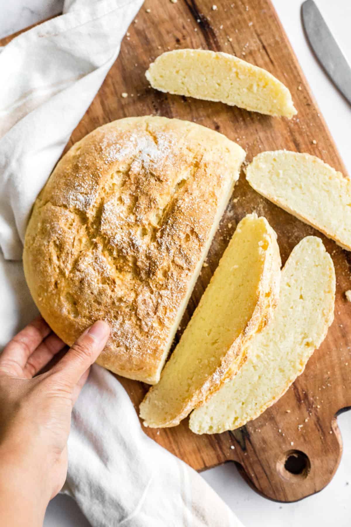 Hand reaching for gluten-free artisan bread on wooden board.