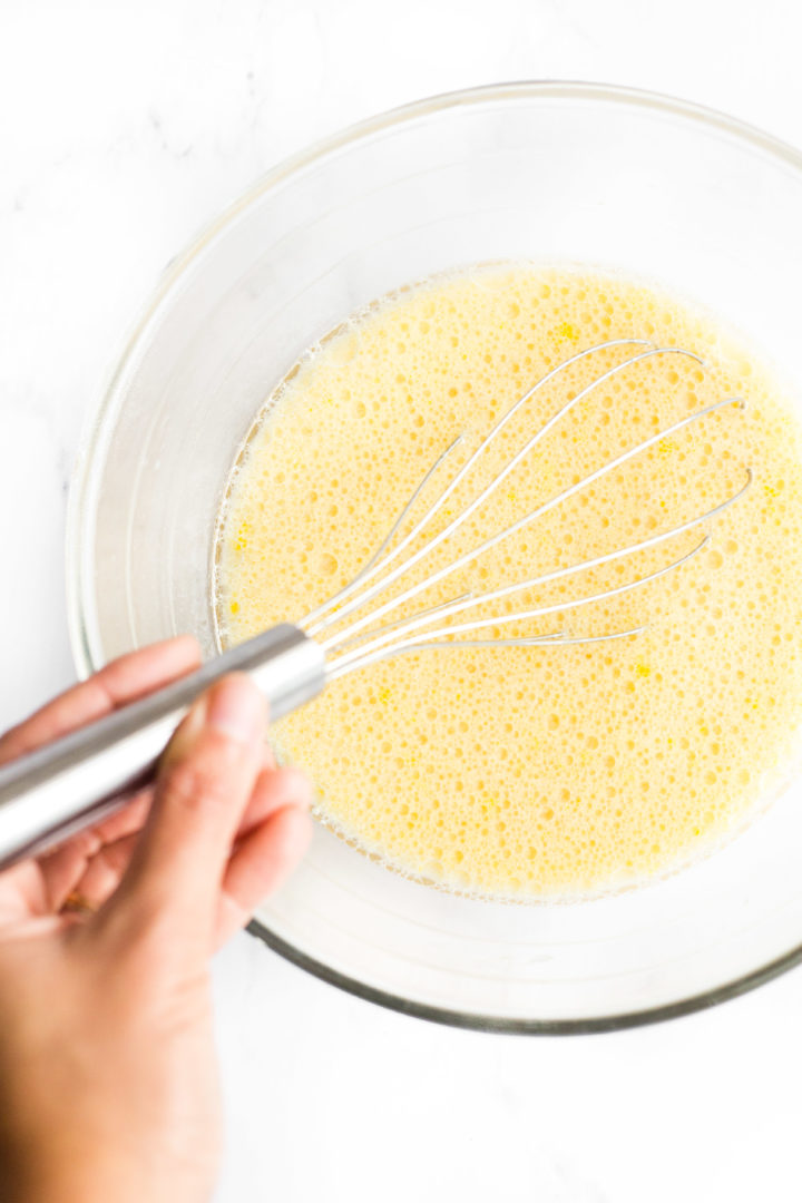 Whisking yellow liquid mixture in a glass mixing bowl.