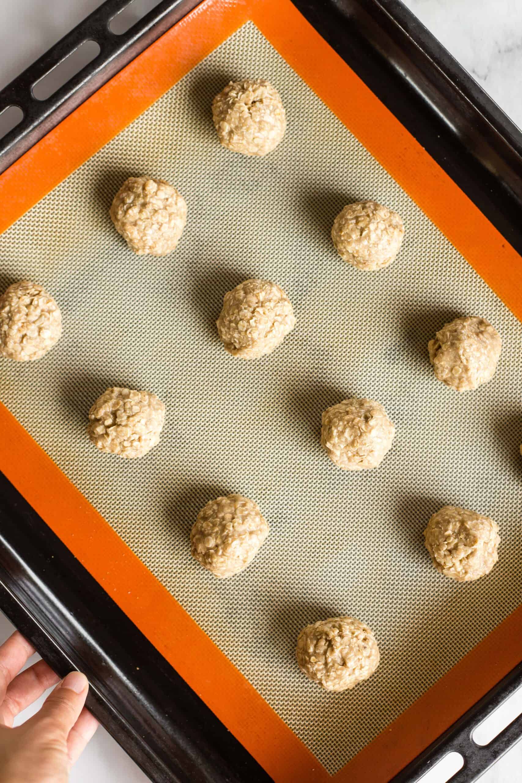 Holding a silpat-lined cookie sheet with cookie dough balls.