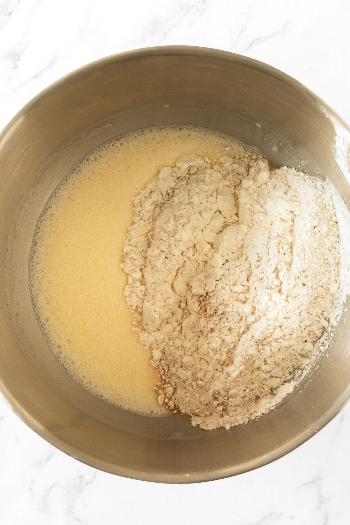 Flour mixing and pale yellow liquid mixture in metal bowl