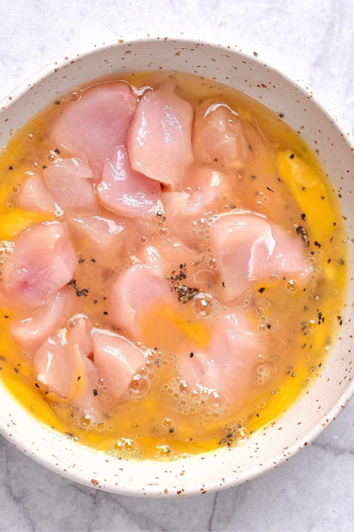 Orange chicken gluten-free recipe Chicken pieces in an egg mixture in a white bowl.