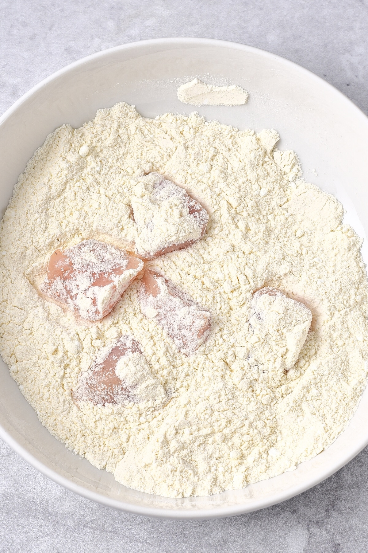 GF Orange Chicken (Dairy-Free) Coating chicken pieces in a bowl of flour.