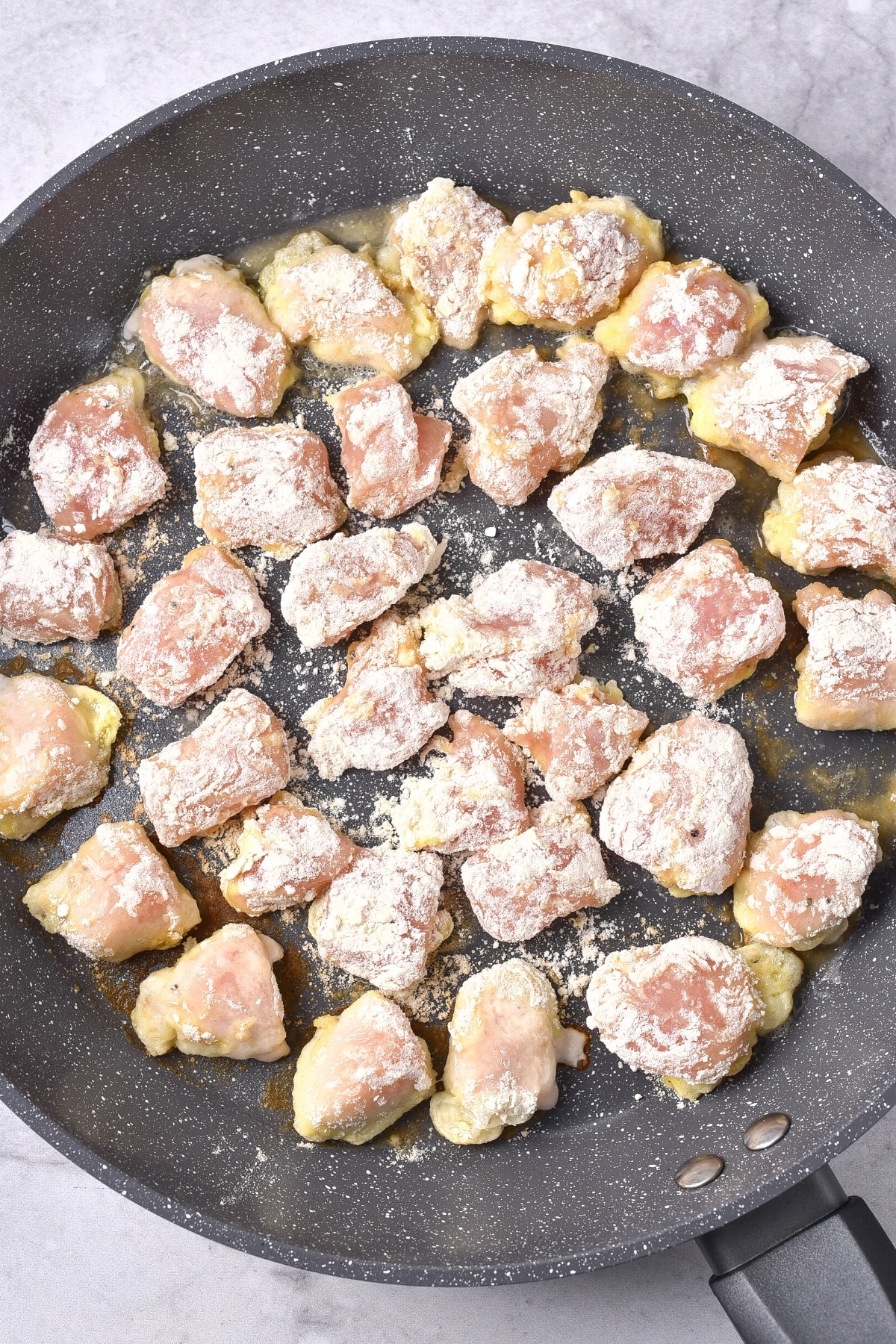 Gluten-Free Dairy-Free Orange Chicken Flour-coated chicken pieces in a skillet.