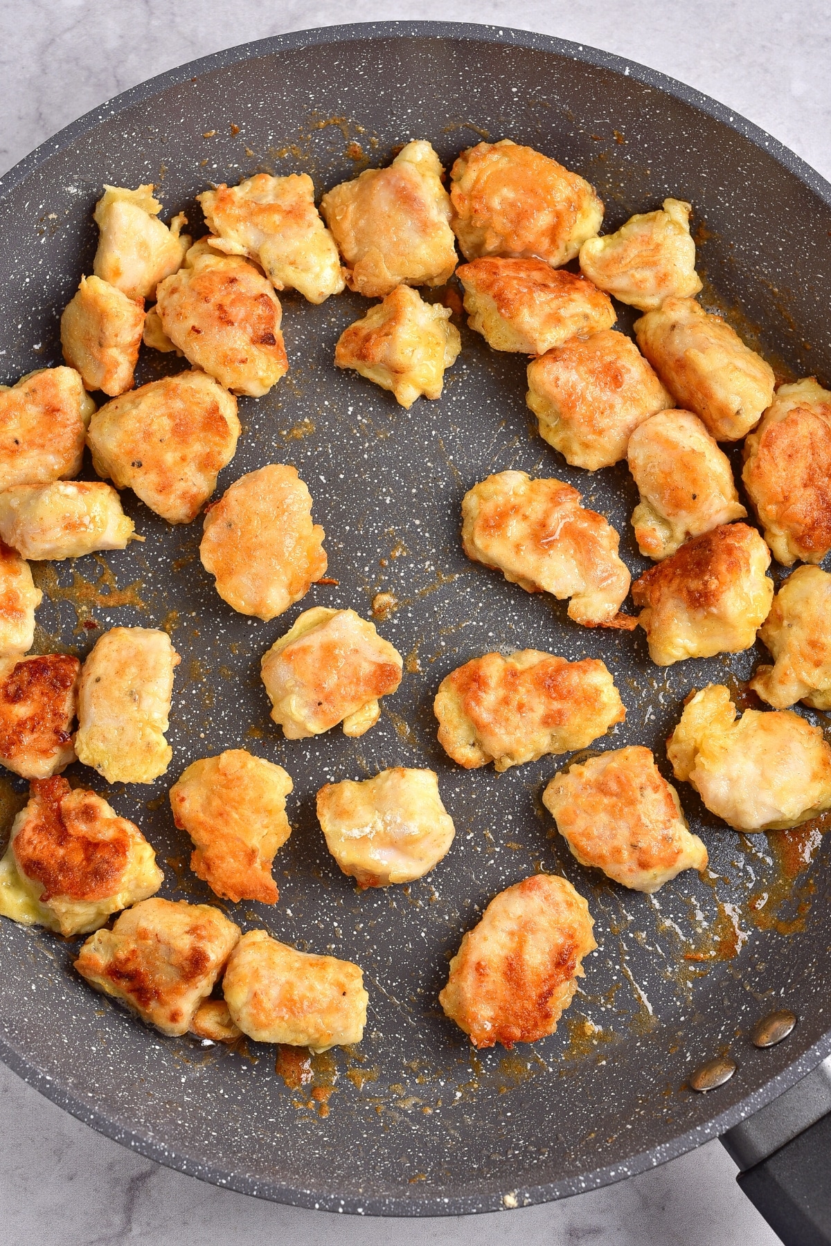 Easy Gluten-Free Orange Chicken Recipe (Dairy-Free) Golden brown fried chicken pieces in a large skillet.