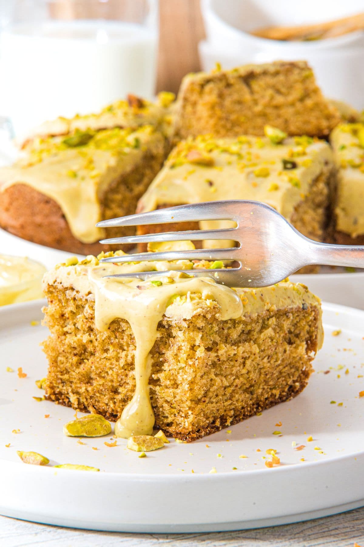 A fork cutting into a piece of gluten-free pistachio cake on a plate.