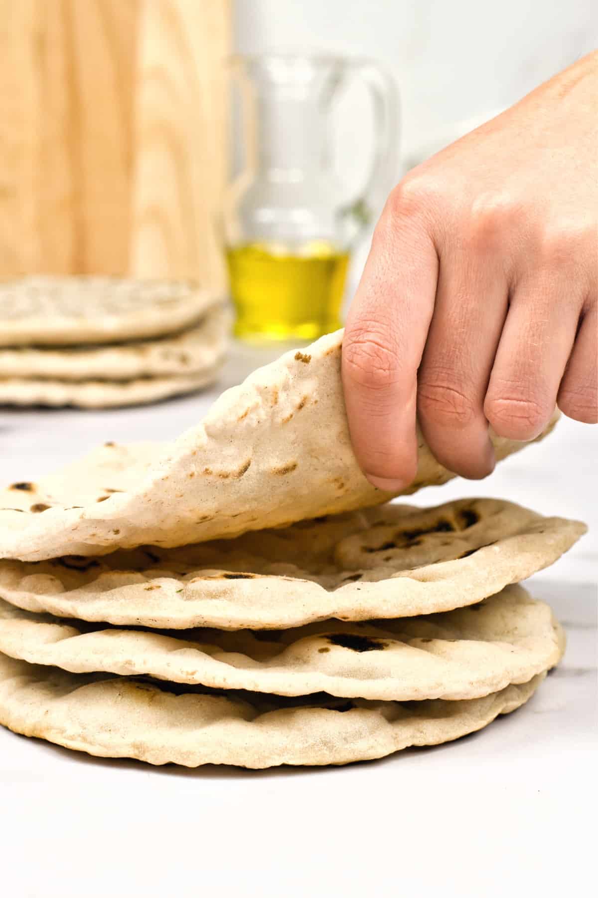 Hand holding up a pita bread from a stack of pitas.
