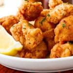 A bowl of gluten-free popcorn chicken and a lemon wedge.