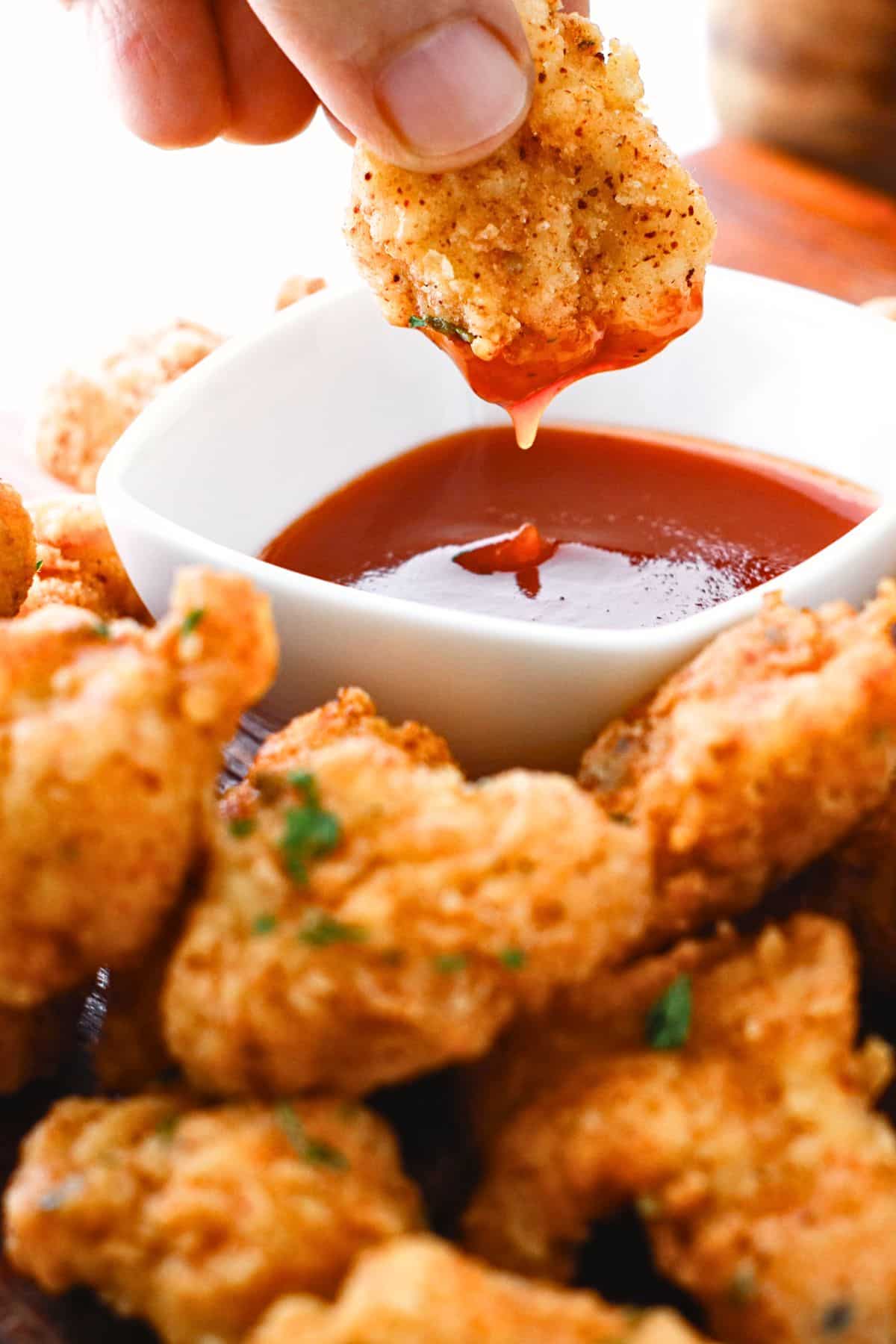 Dipping gluten-free popcorn chicken in a bowl of chili sauce.