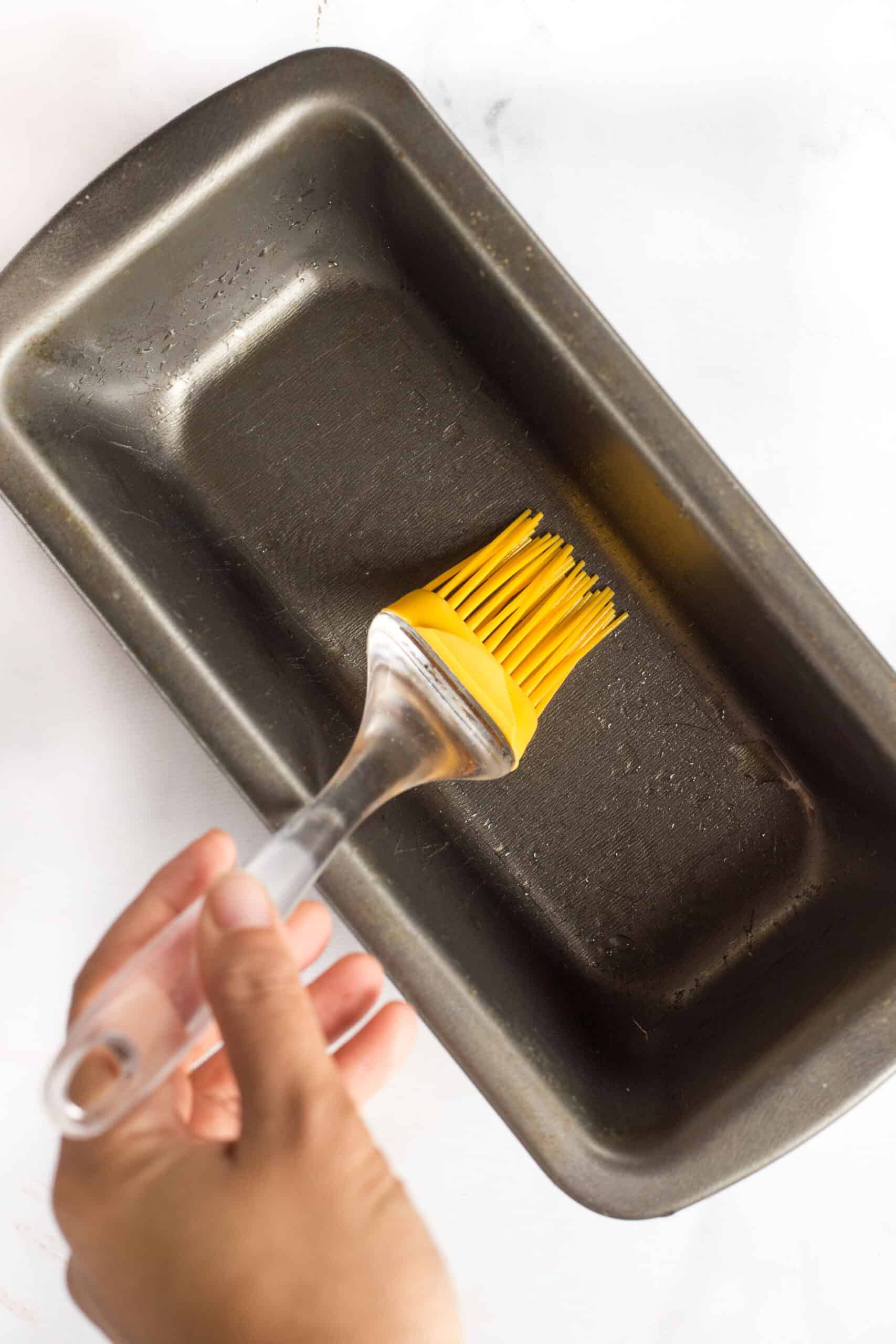 Using a yellow silicon brush to grease a metal loaf pan.