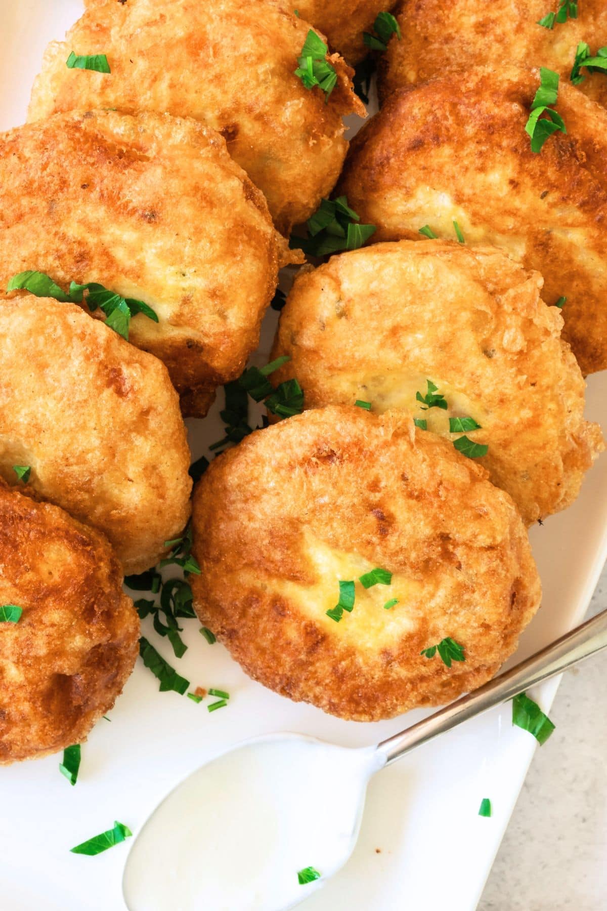 Top down view of potato patties and a spoon with white sauce.