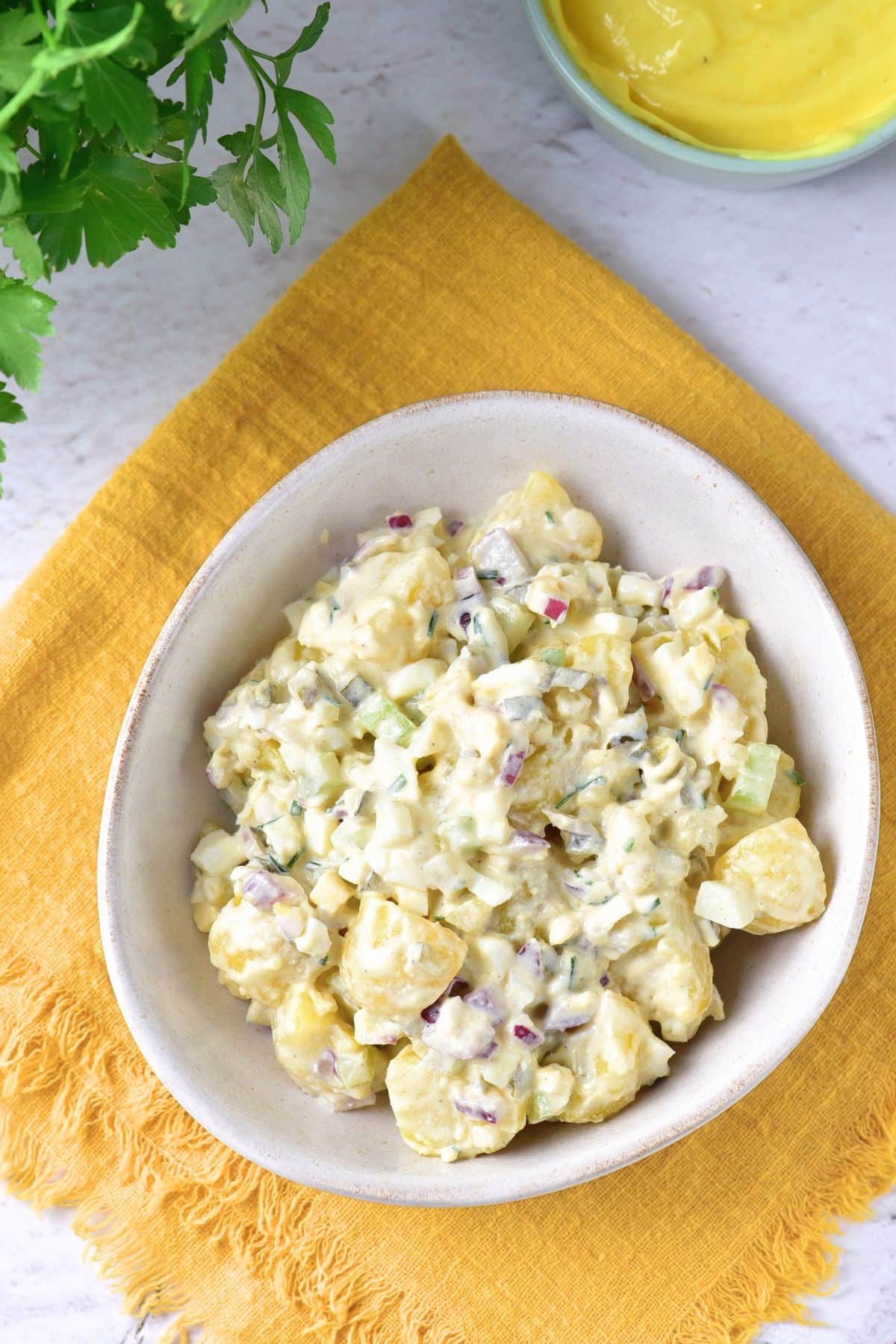 Top down view of bowl of potato salad on yellow cloth.