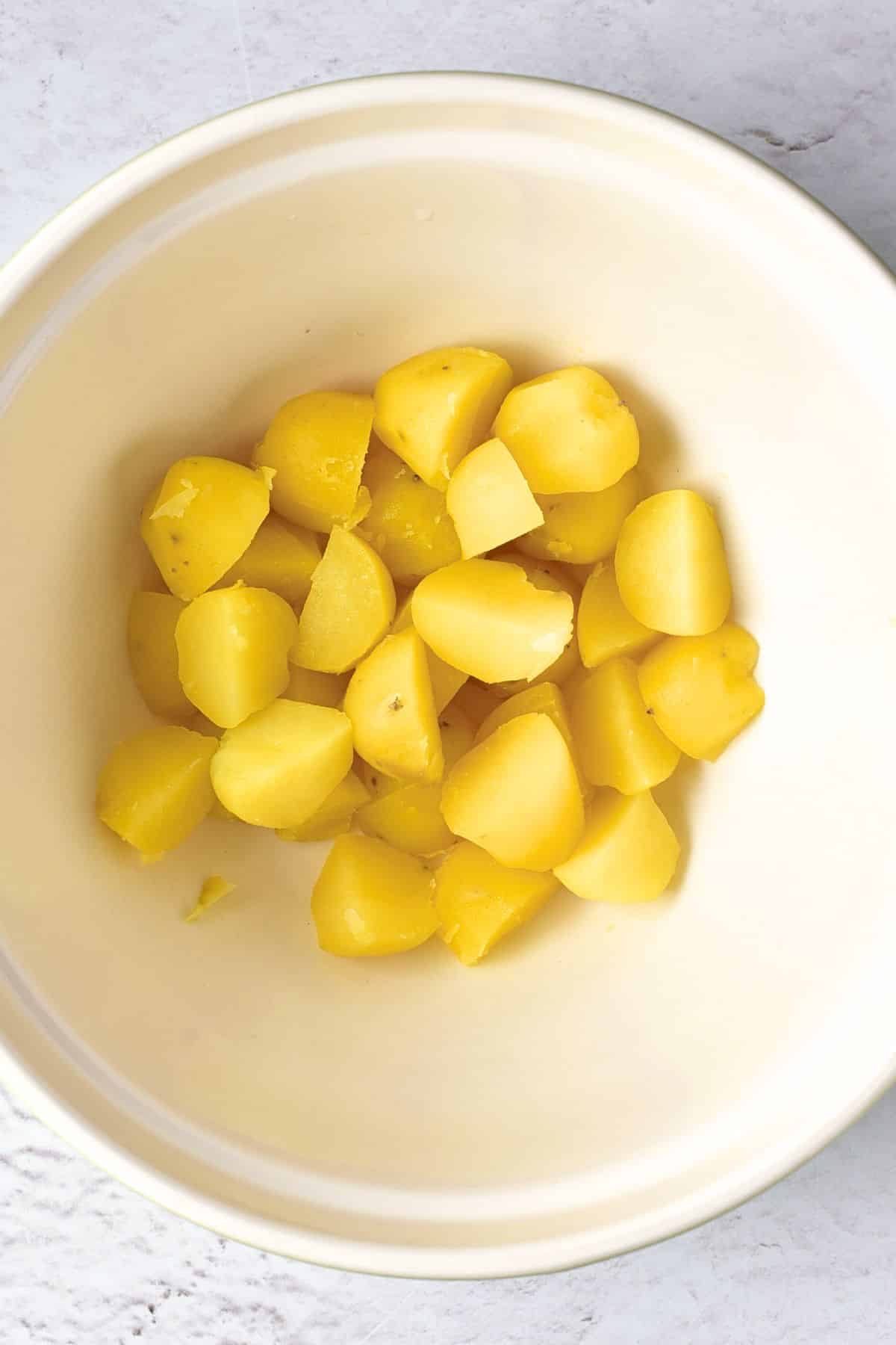 Cooked and cut potatoes in white bowl.