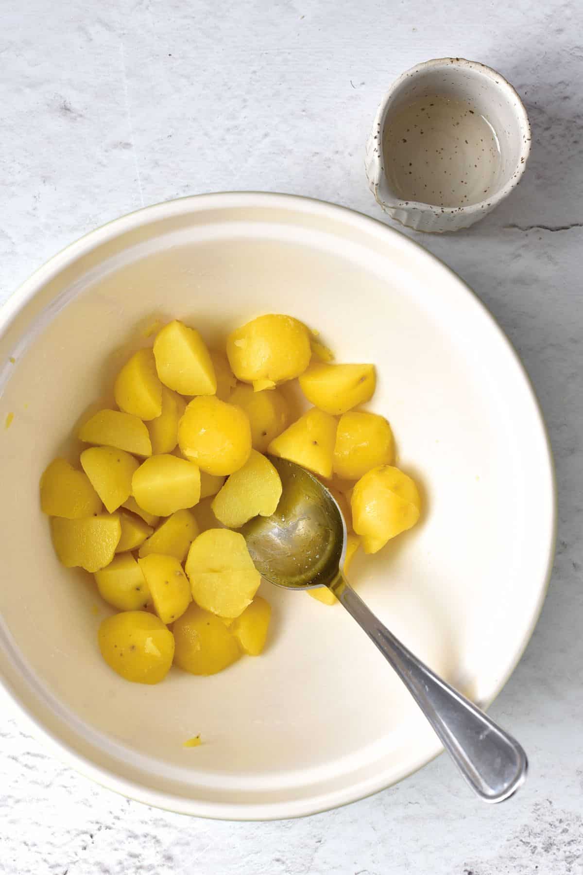 Mixing cooked potatoes and vinegar in white bowl.