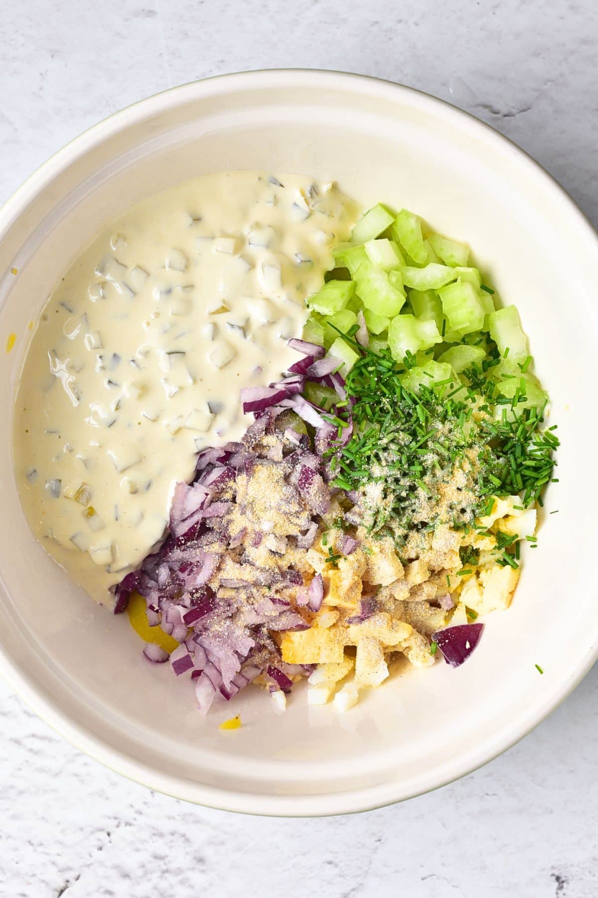 A bowl with chopped onions, celery, mayonnaise, chives and eggs.