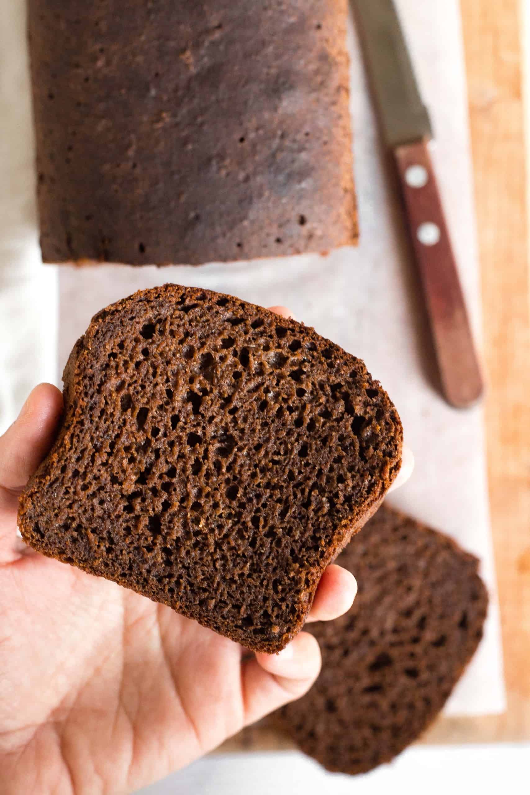 Holding up a slice of gluten-free pumpernickel bread to show the texture.