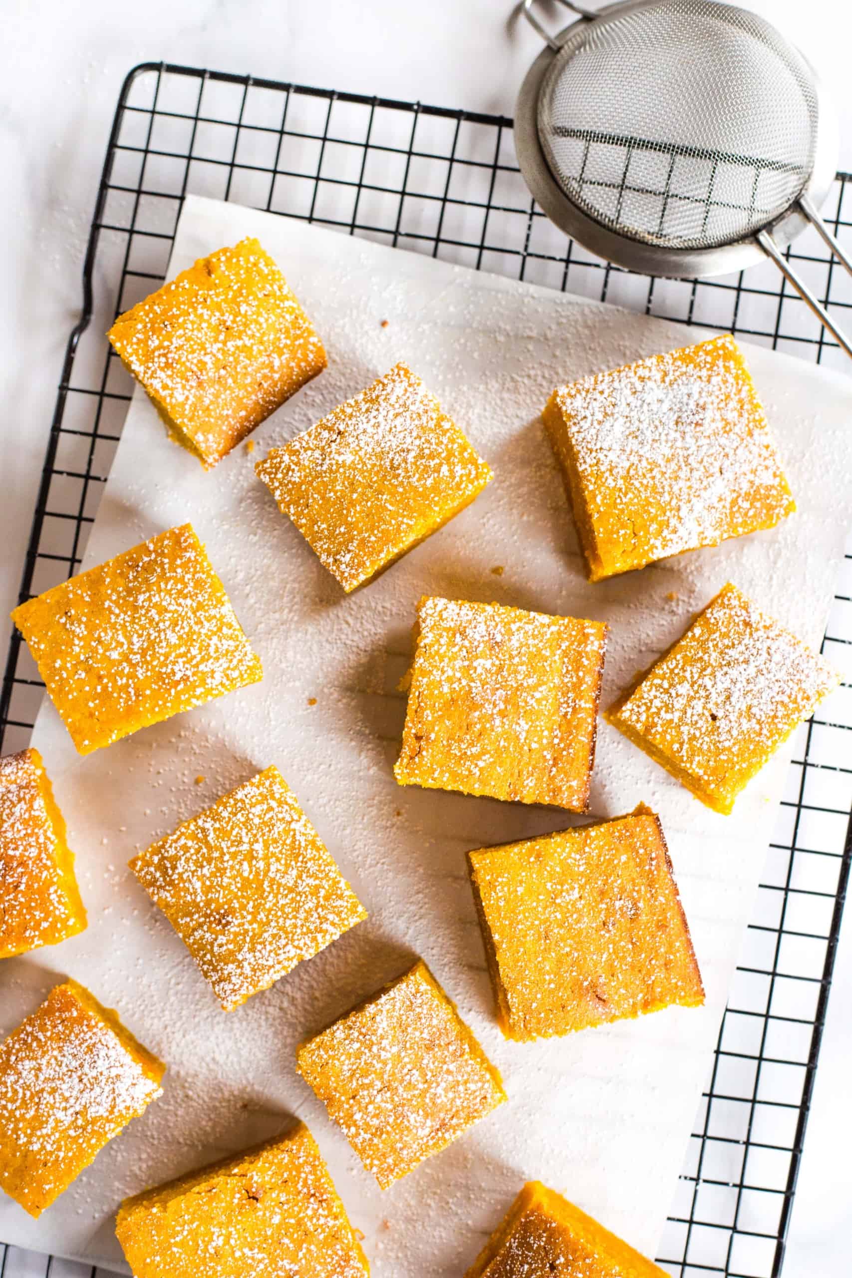 Gluten-free pumpkin squares sprinkled with powdered sugar on parchment-lined cooling rack.