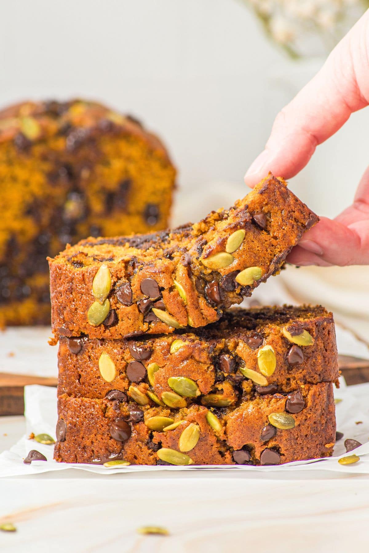 Hand reaching for a slice of gluten-free pumpkin bread with chocolate chips.