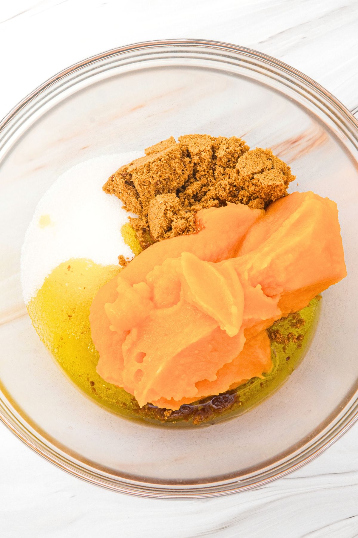 Sugar, pumpkin puree, and oil in glass bowl.