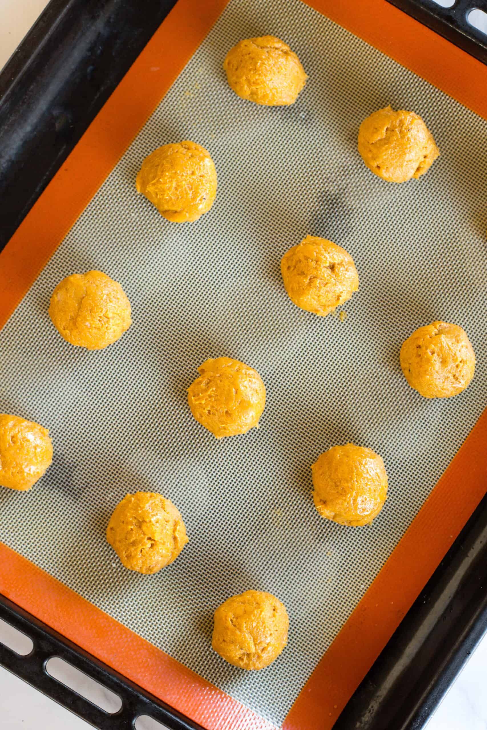 Pumpkin dough balls on a silpat-lined baking sheet.
