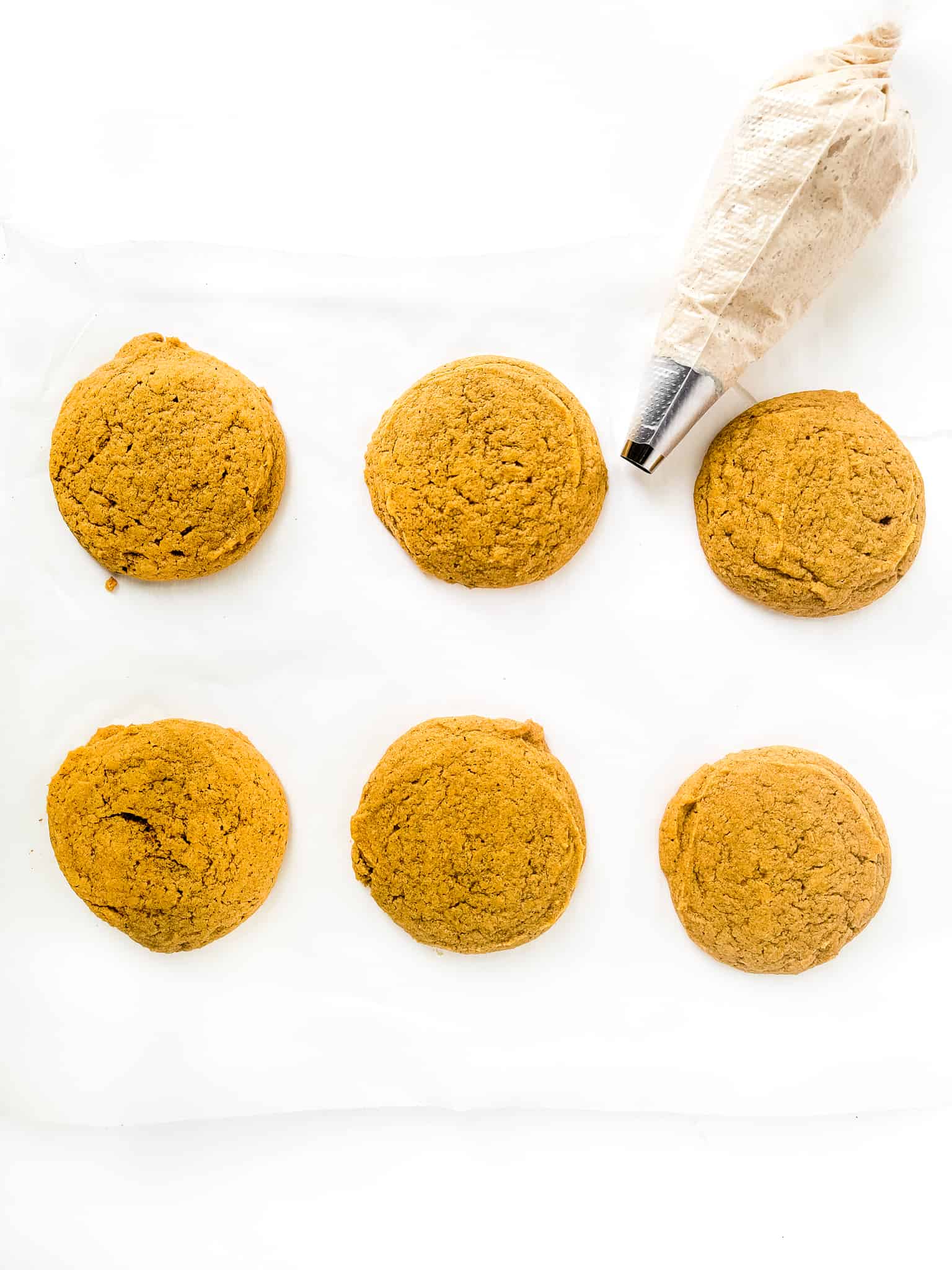 Freshly baked gluten-free pumpkin cookies with a piping bag filled with frosting.
