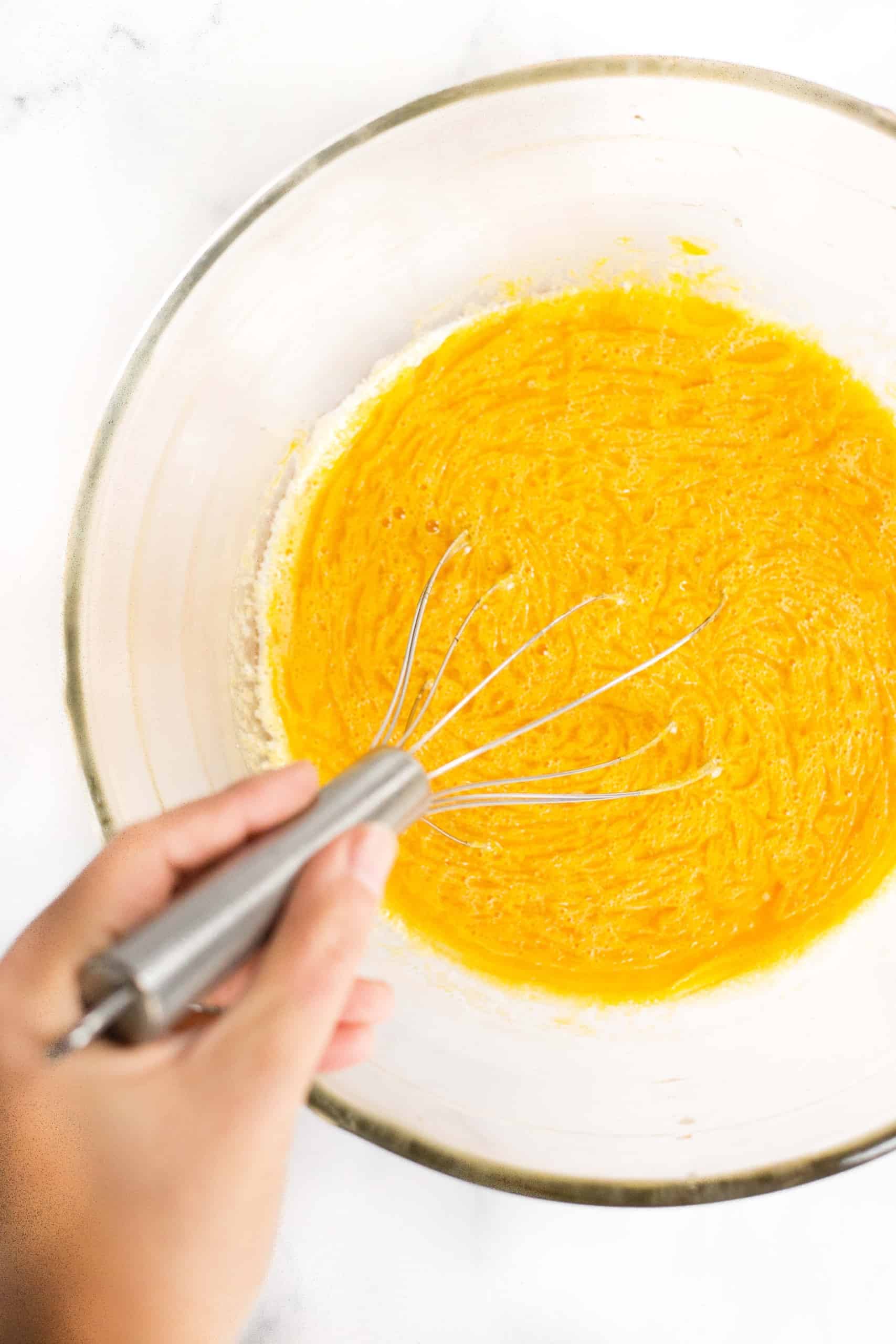 Mixing yellow-orange liquid in glass bowl.