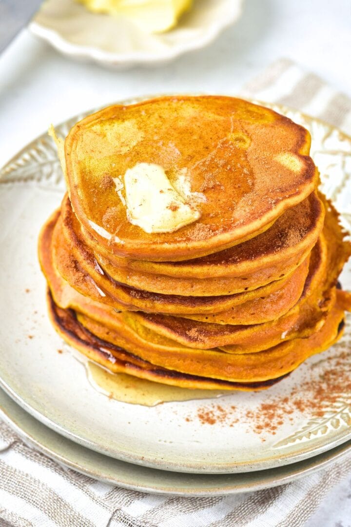 A stack of gluten-free pumpkin pancakes topped with butter on plate