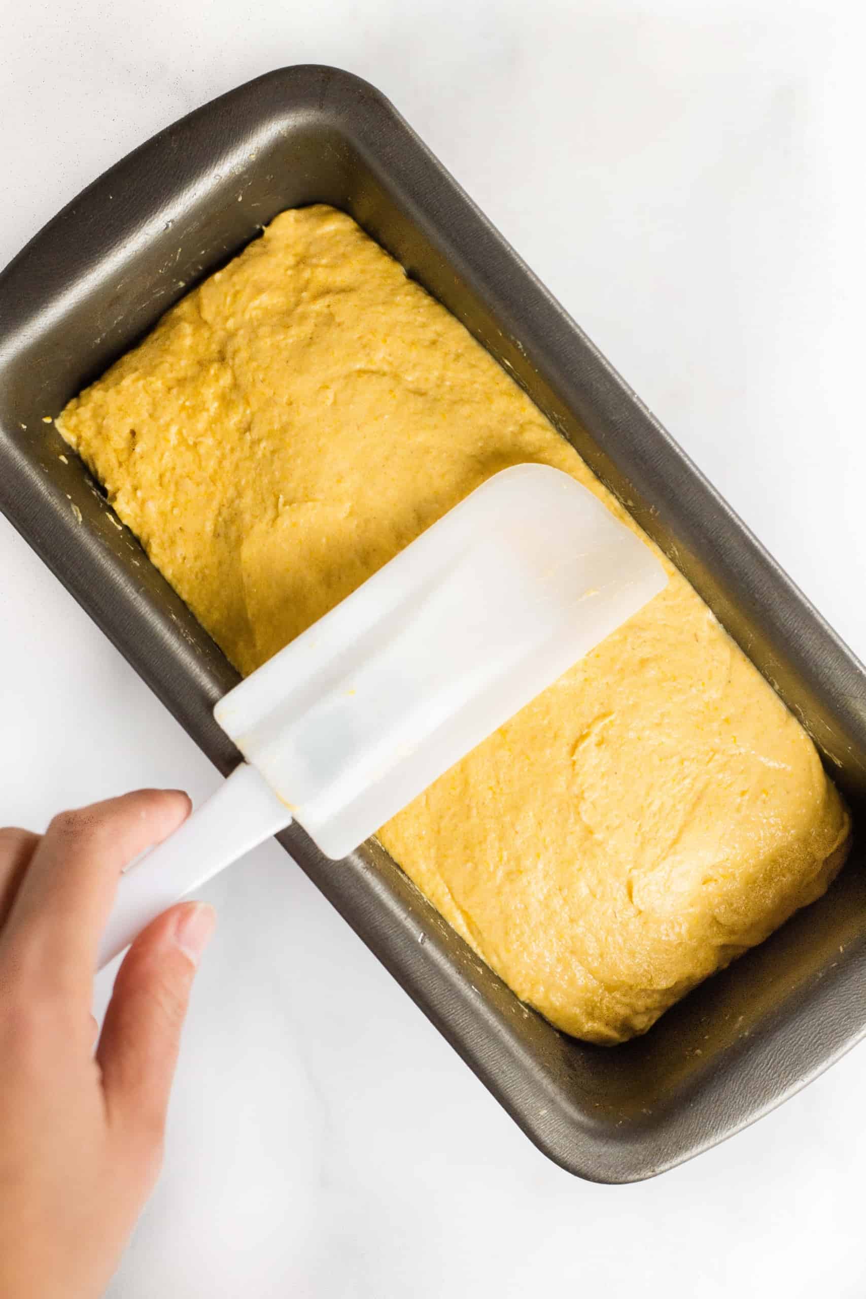 Smoothing out top of pumpkin bread dough with wet spatula.
