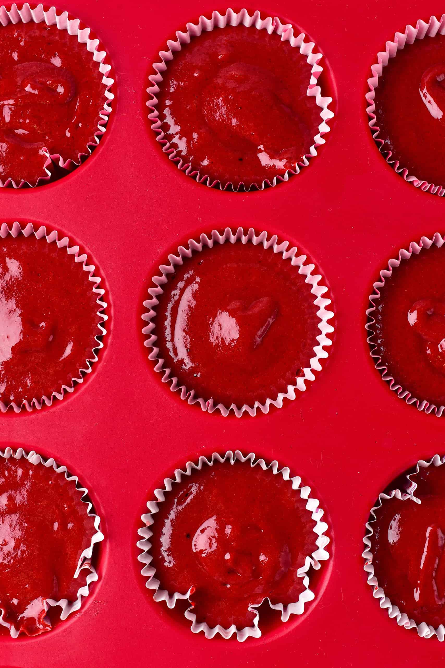 Red velvet cupcake batter in lined muffin tin.