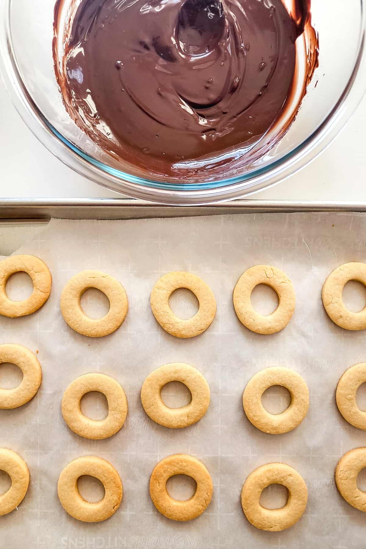 A parchment-lined tray with cookies and a bowl of melted chocolate.