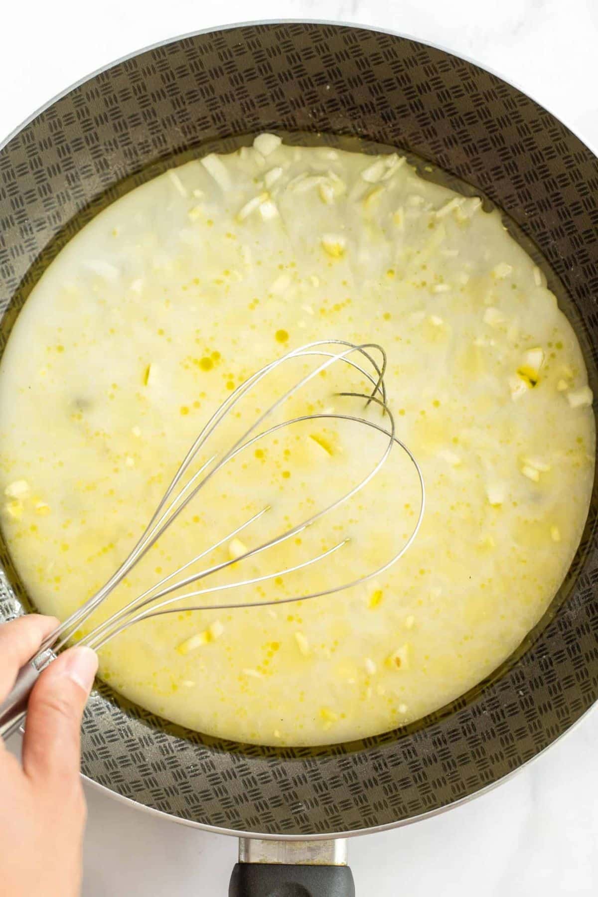 Whisking minced garlic in pale yellow liquid mixture.