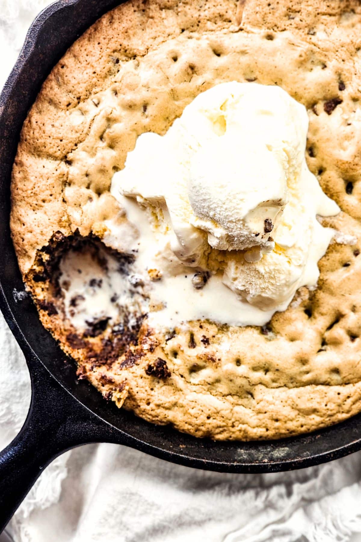 Half-eaten gluten-free cookie skillet topped with vanilla ice cream.