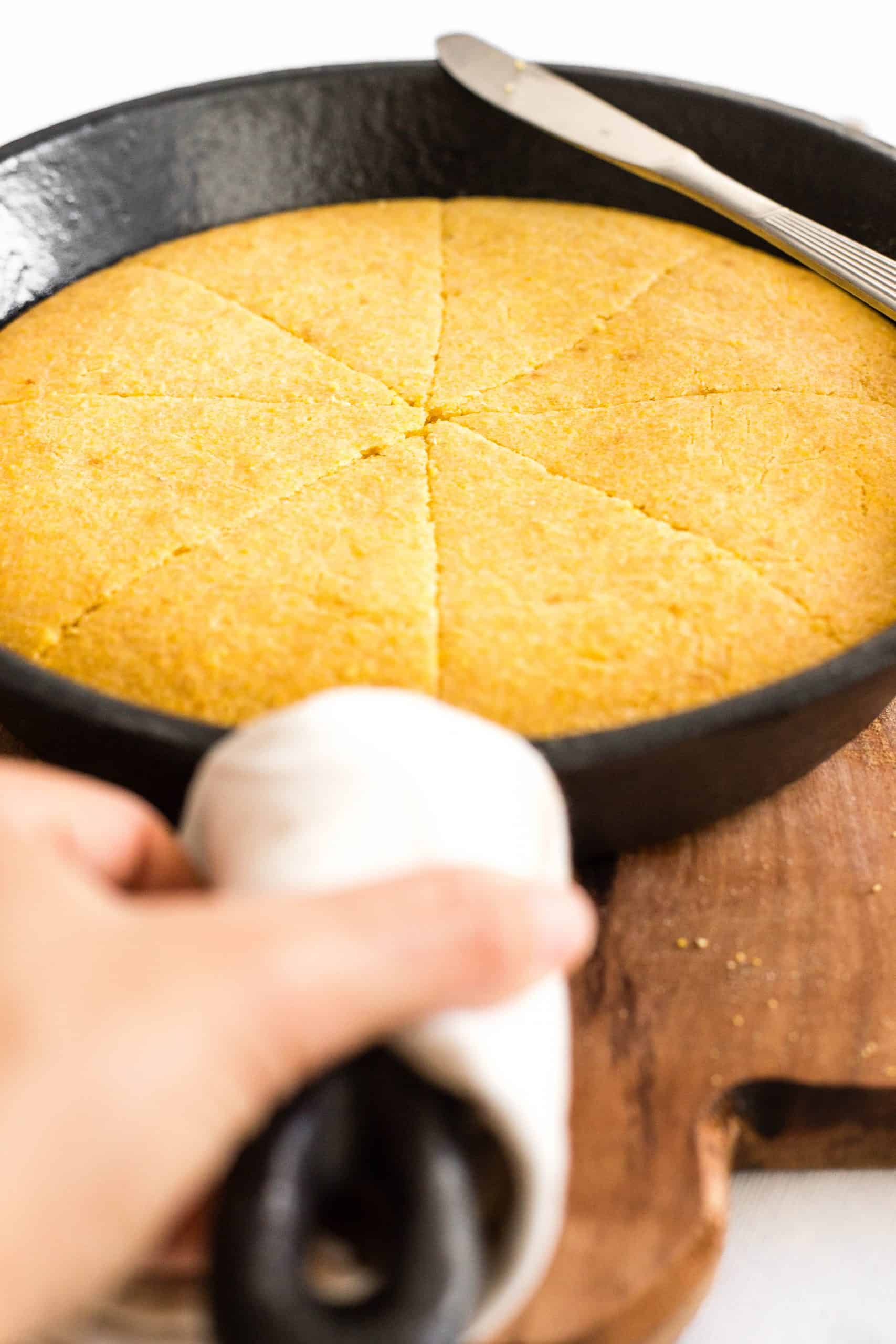 Hand reaching for a skillet with gluten-free cornbread.