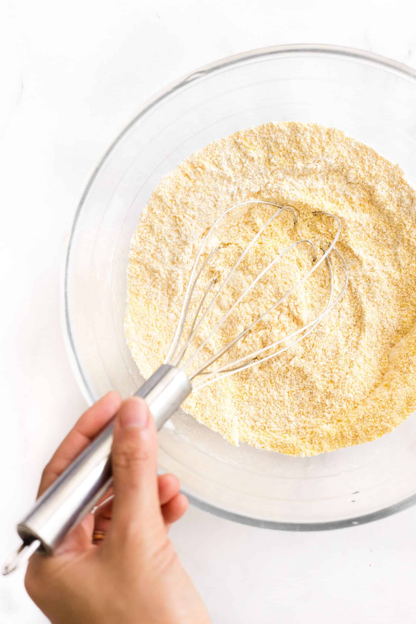 Hand whisking dry ingredients in a glass mixing bowl.