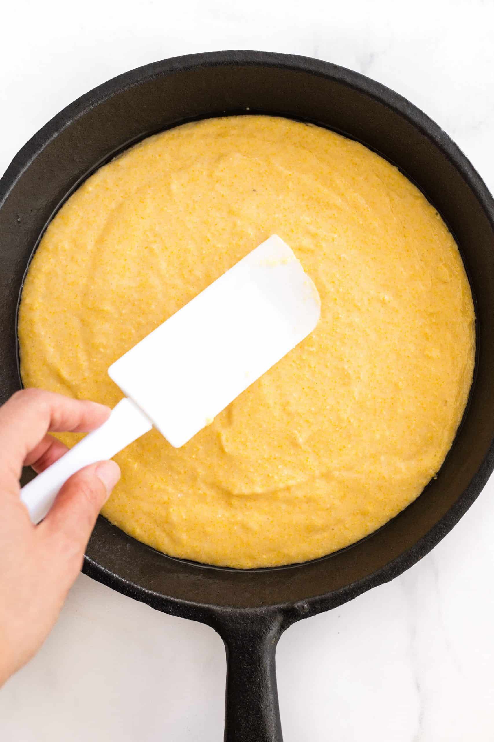 Using a spatula to smooth out the batter in a cast iron skillet.